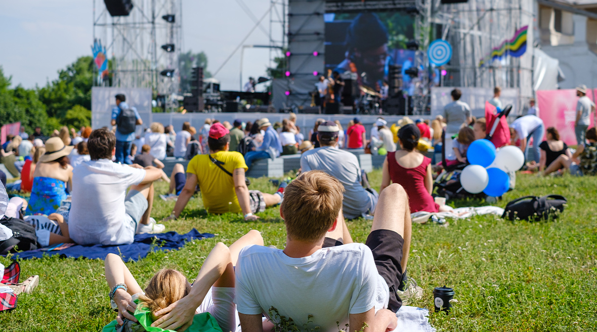 couple laying on green grass at an open air music festival with a stage in the distance